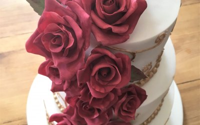 Sugar roses cover this three tier cake with additional gold decorations on each tier. 