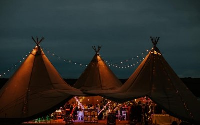 A triple tipi set up, glowing against the night sky in Cornwall.