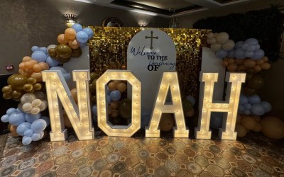 Personalised christening backdrop with the name NOAH in 4ft light up letters, 3 sailboards with one thats personalised, balloons and a sequin wall! This customer went all out with their sons christening!