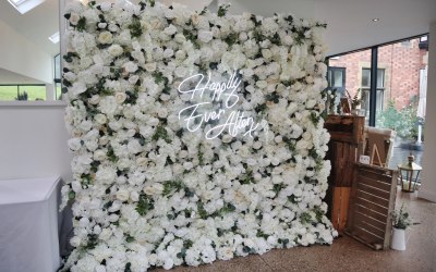 White and nude wedding flower wall backdrop with foliage and neon sign