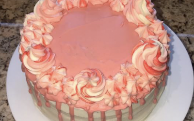 A red velvet sponge with vanilla buttercream, white chocolate drip and 3 tone pink buttercream icing swirls.