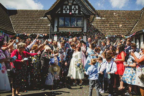 Group wedding picture with newly weds and guests in front of old Tudor building. Image courtesy of Camera Hannah Photography