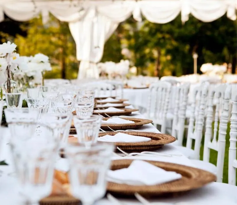 Table decorations and plates laid on white table at an outdoor wedding