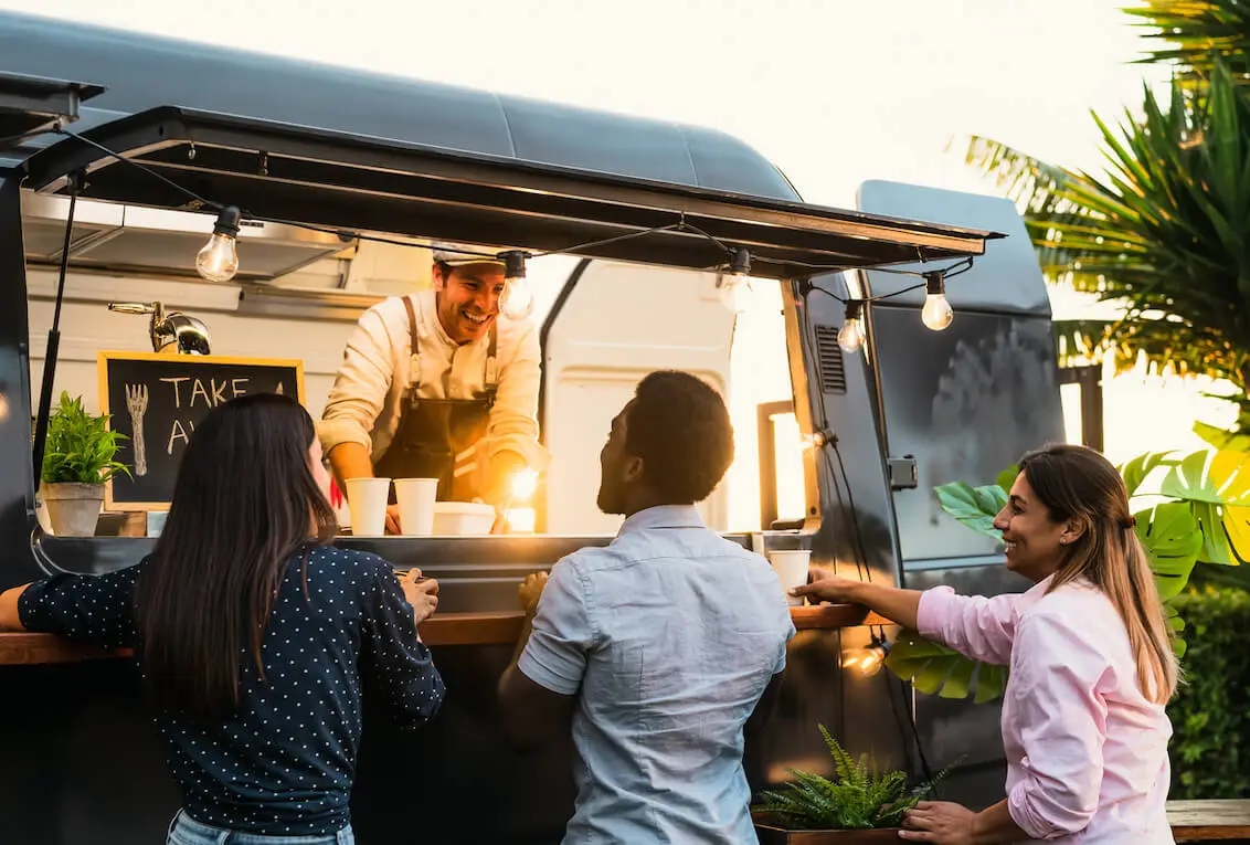 Three people ordering and being served at a food van at an outdoor event