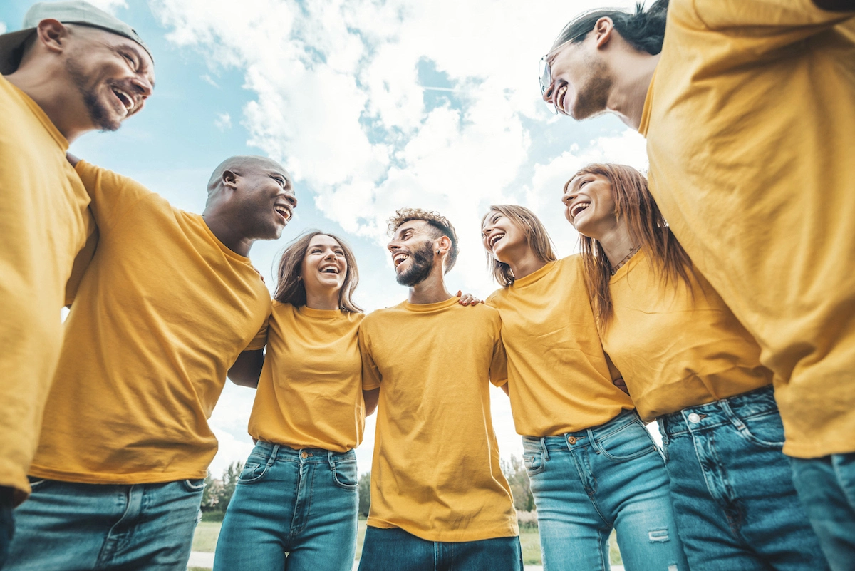 A group of 7 young work colleagues wearing yellow t-shirts in a team huddle