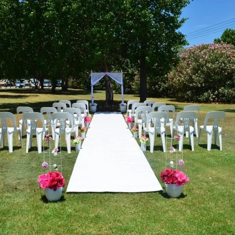 Image of an outdoor wedding reception with rows of chairs and a white carpet aisle
