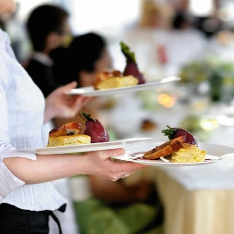 Image of a female waitress carrying two plates of food to a wedding table