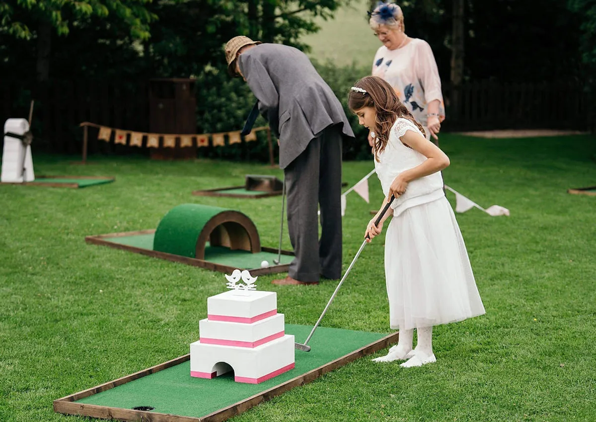 A small girl playing crazy golf on the lawn at a summer wedding