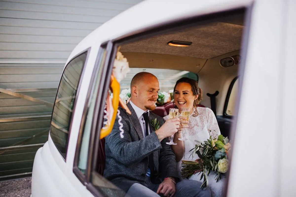 Newly wedded couple enjoying drinks in the back of a white taxi for their wedding