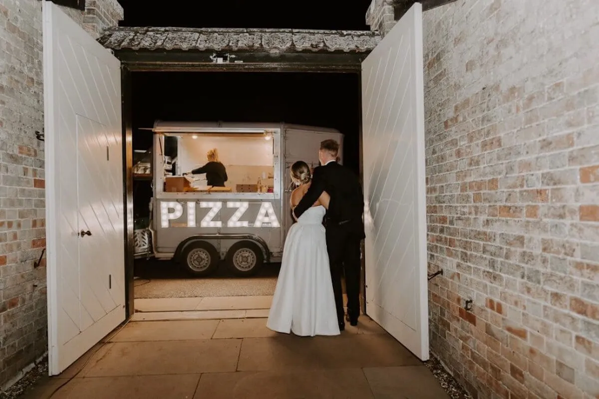 Photo of loving wedding couple standing in front of pizza van at their wedding
