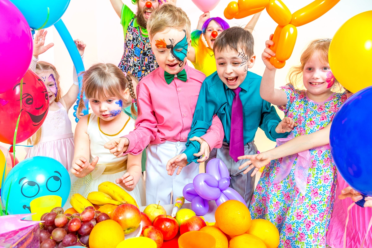 A group of colourful young kids playing with balloons and wearing face paint