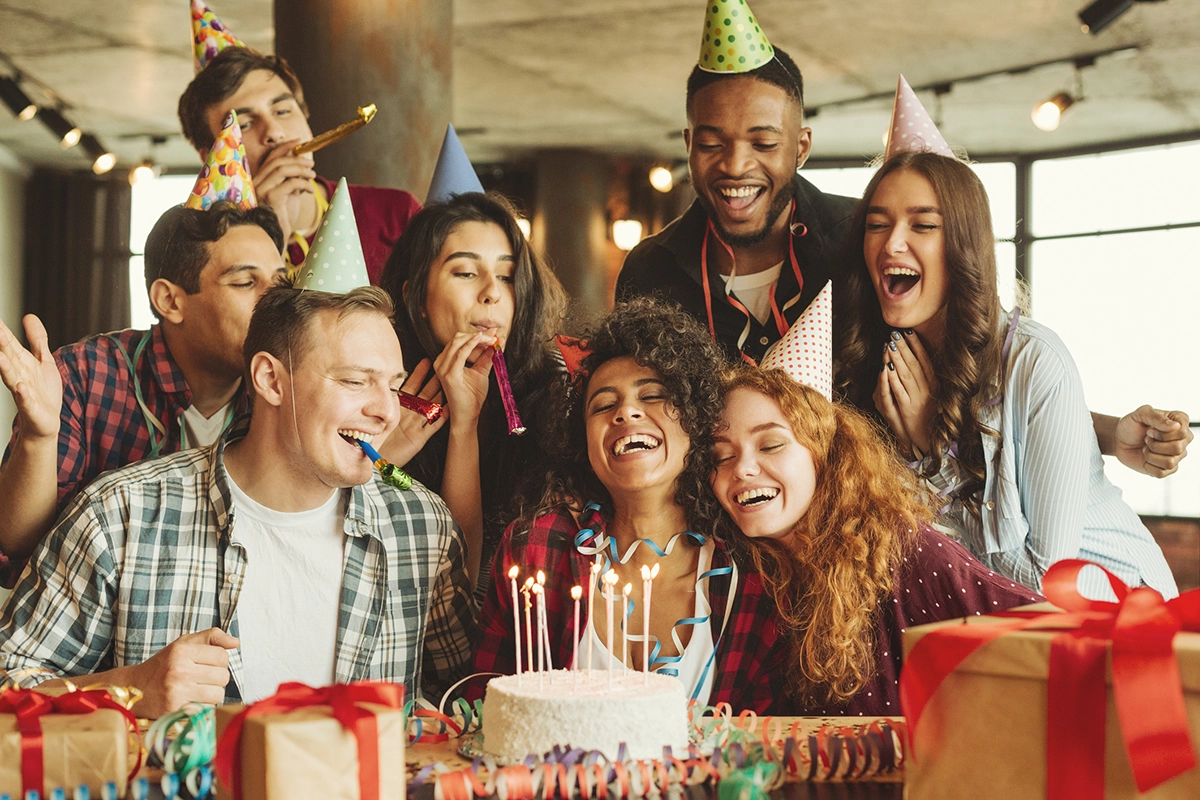 A group of friends celebrating a birthday with birthday cake, presents and hats